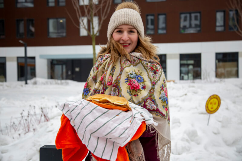 Smiling Woman Colorful Shawl Winter Hat Holds Stack A smiling woman in a colorful shawl and winter hat holds a stack of pancakes in the snow.