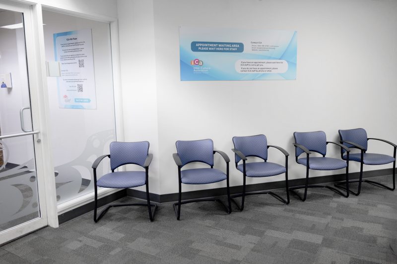 Waiting Area Five Blue Chairs White Wall Sign A waiting area with five blue chairs in front of a white wall with a sign.