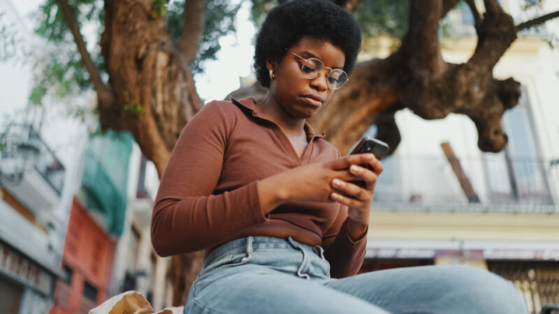 Young Black Woman Afro Hairstyle Glasses Looking Her Young Black woman with afro hairstyle and glasses looking at her phone outdoors.