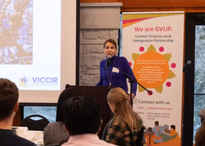 A woman speaks at a podium in front of a banner for the Greater Victoria Local Immigration Partnership.