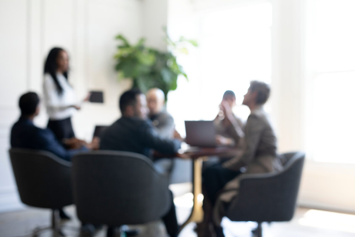 Blurred image of a business meeting with several people around a table.