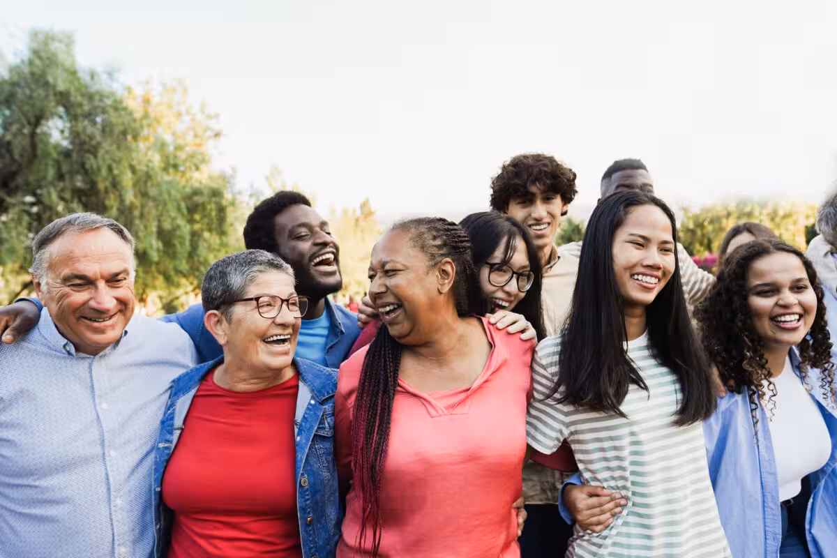 A diverse group of people of various ages and ethnicities laughing together outdoors.