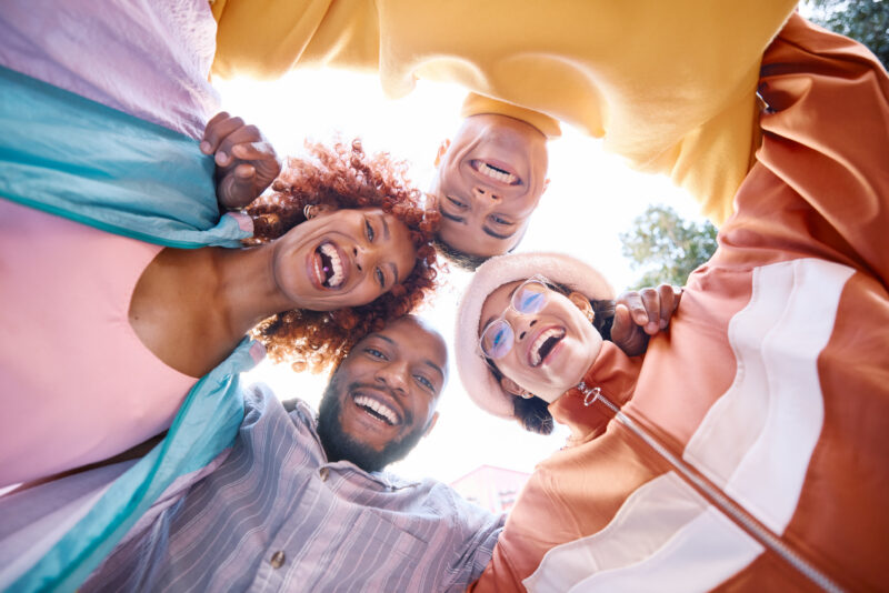 Four friends laugh together in a circle from a low angle, looking up at the camera.
