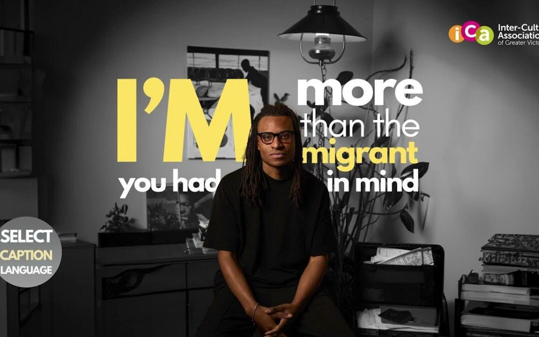 A man with dreadlocks and glasses sits looking forward, with text on screen reading "I'M more than the migrant you had in mind.