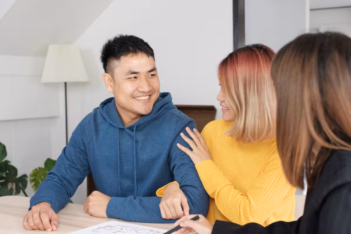 Couple Smiles While Looking Architectural Plans Third Person A couple smiles while looking at architectural plans with a third person.